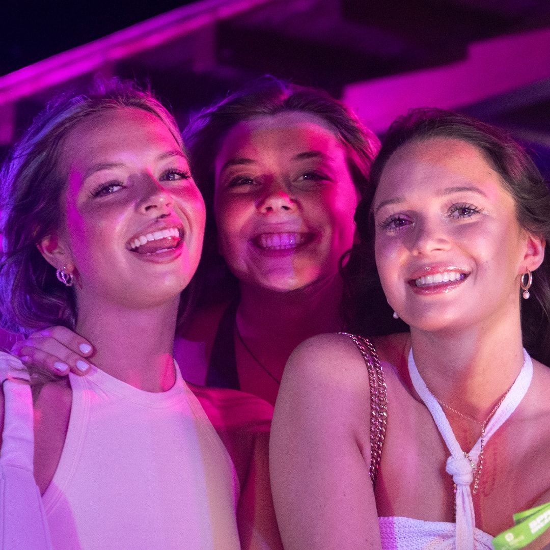 Three friends laughing together under pink and purple neon lights at La Vaquita Cancún
