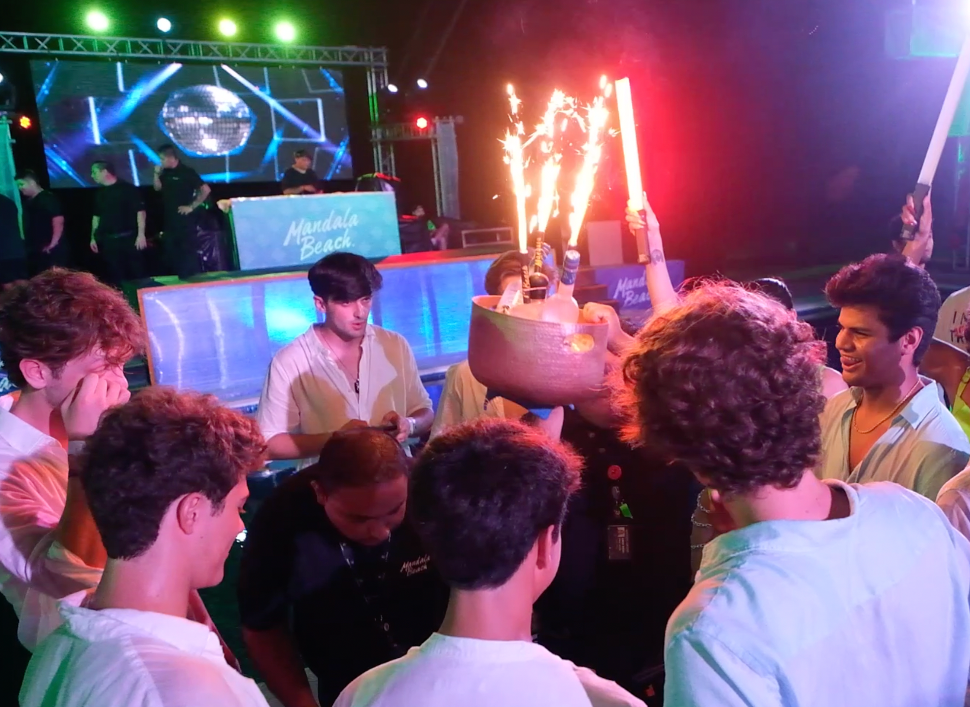 Group celebrating with sparklers and a giant cocktail bowl at Mandala Beach during Madness Tour