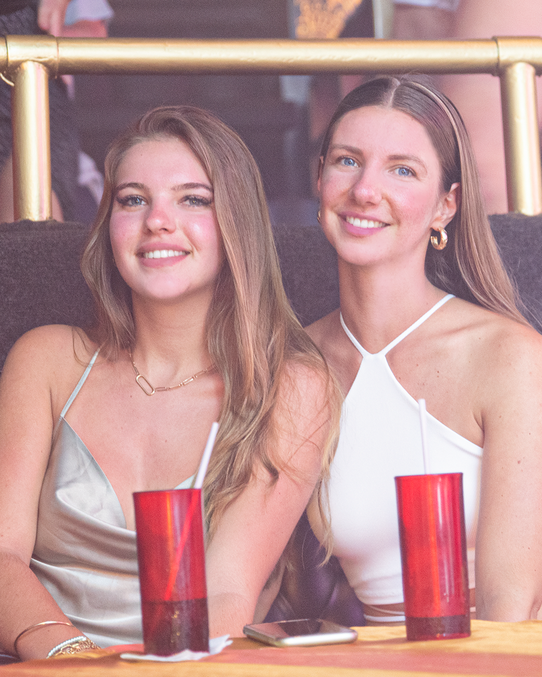 Two women smiling with red drinks at a VIP table inside Mandala Club Cancún