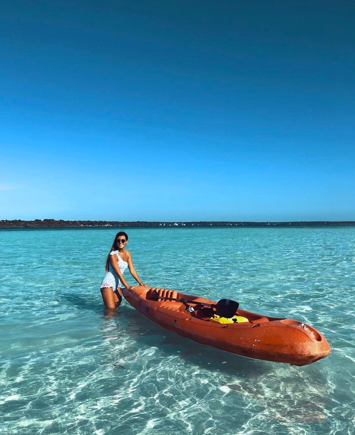 Woman with an orange kayak in the shallow turquoise waters of Bacalar