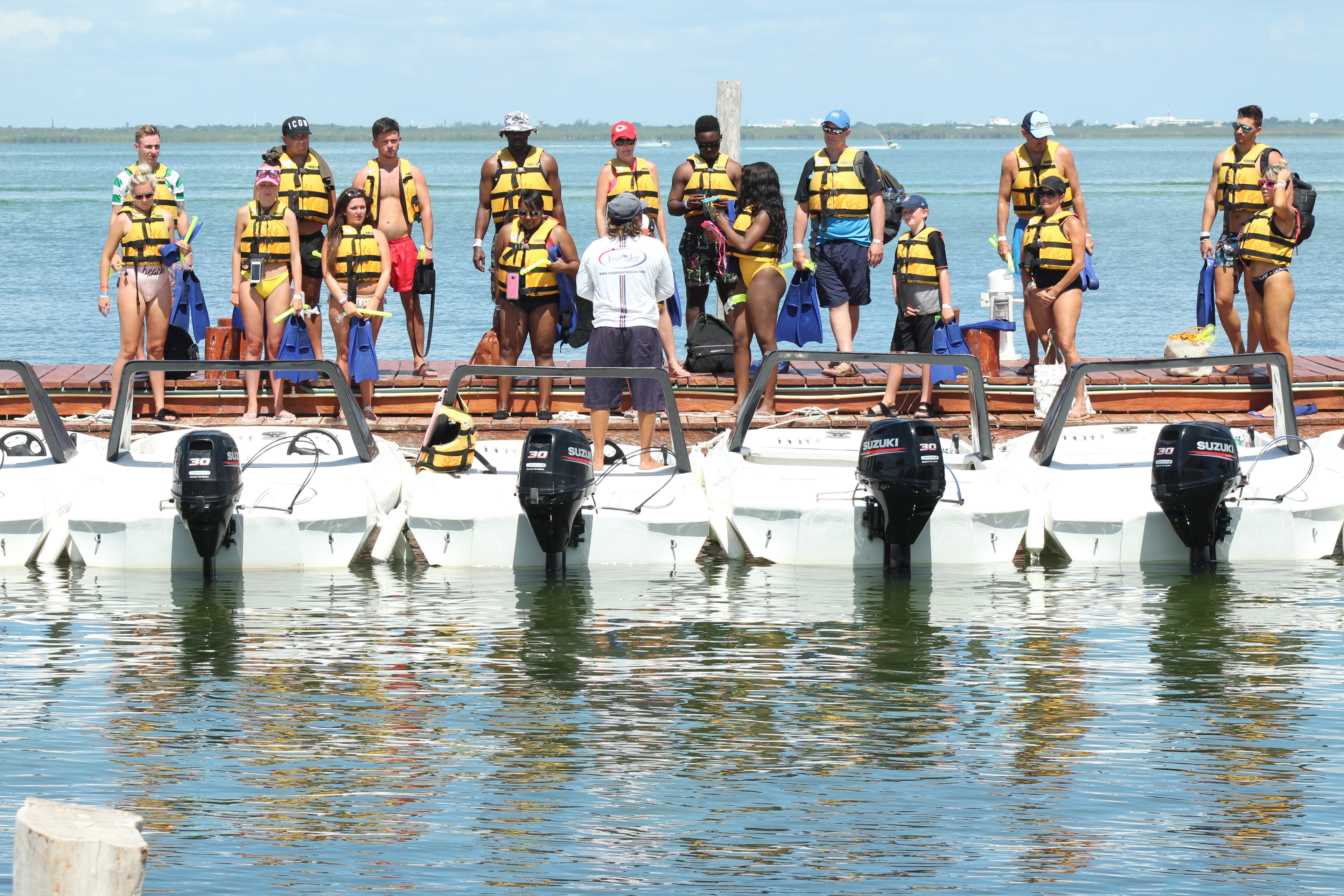 Large group of tourists in life jackets receiving pre-departure safety briefing at the Jungle Tour dock