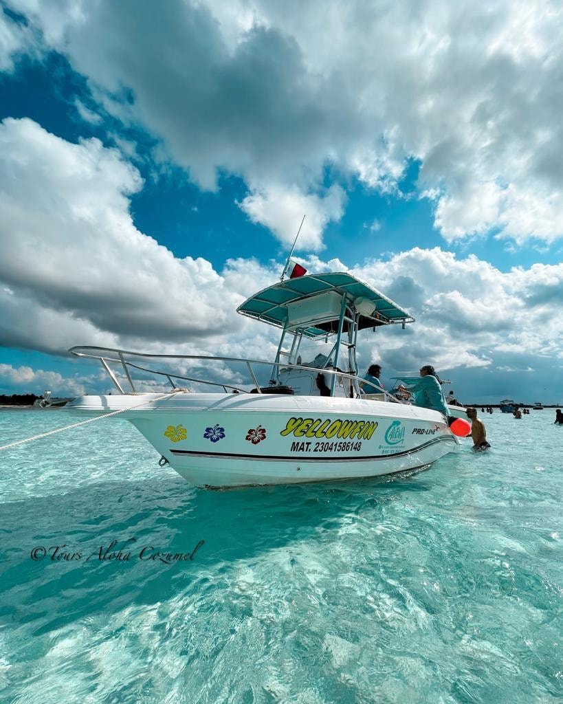 Yellowfin tour boat anchored in brilliant turquoise shallow water under a dramatic cloudy sky in Cozumel