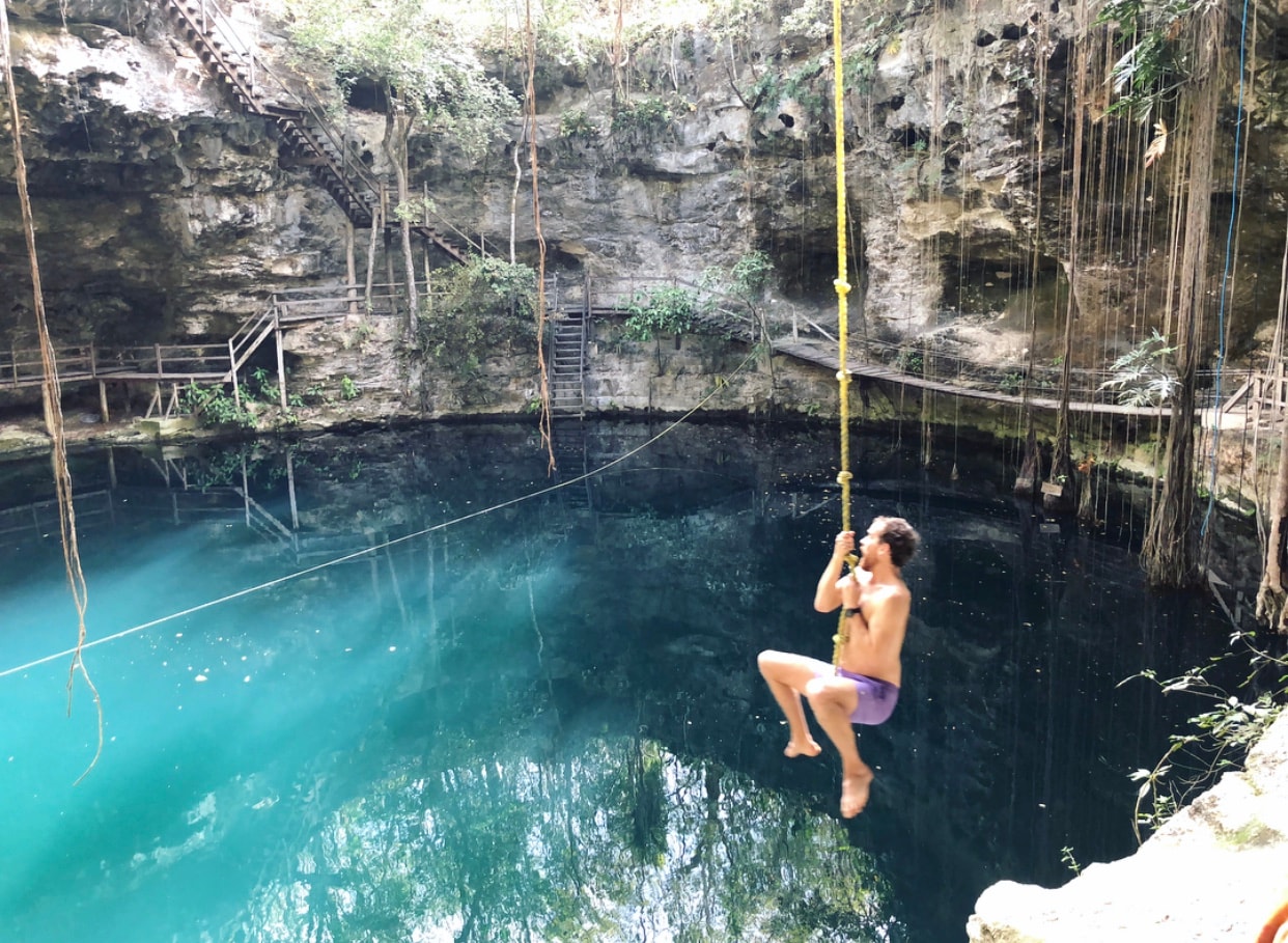 Guest swinging on a rope over the turquoise waters of a cenote near Ek Balam