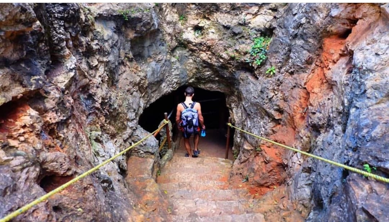 Visitor descending stone steps into a cave cenote entrance with rope railings