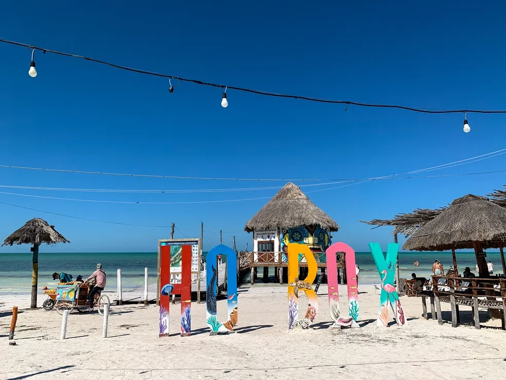 Colourful HOLBOX letter sign on the beach with thatched palapas, string lights and the Caribbean Sea behind