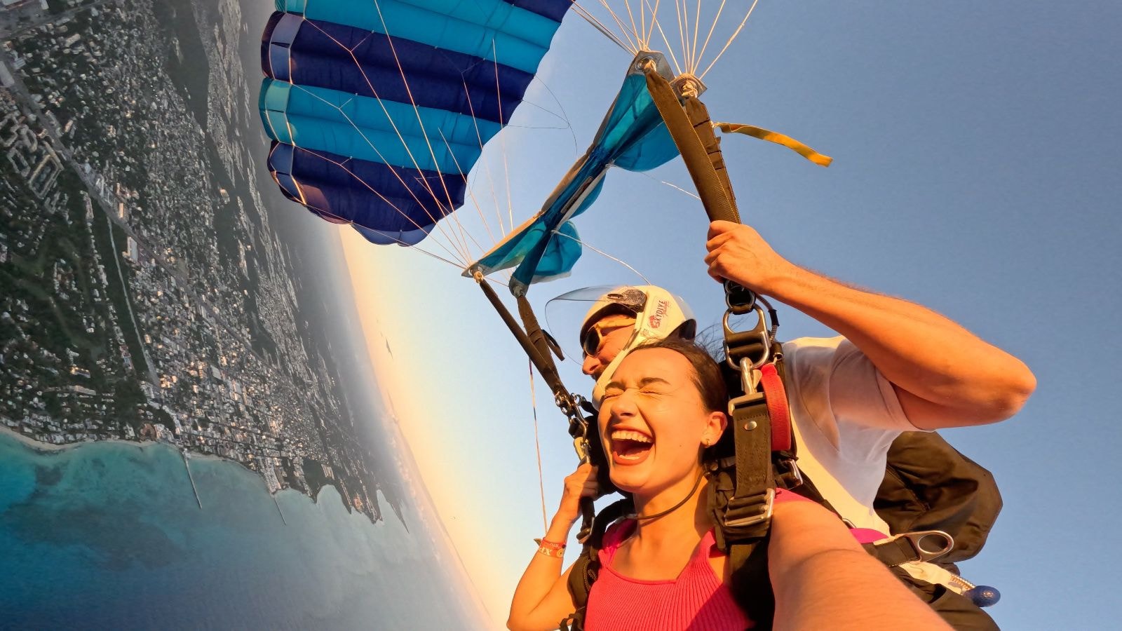 Woman laughing with arms out in freefall under a blue parachute over Playa del Carmen