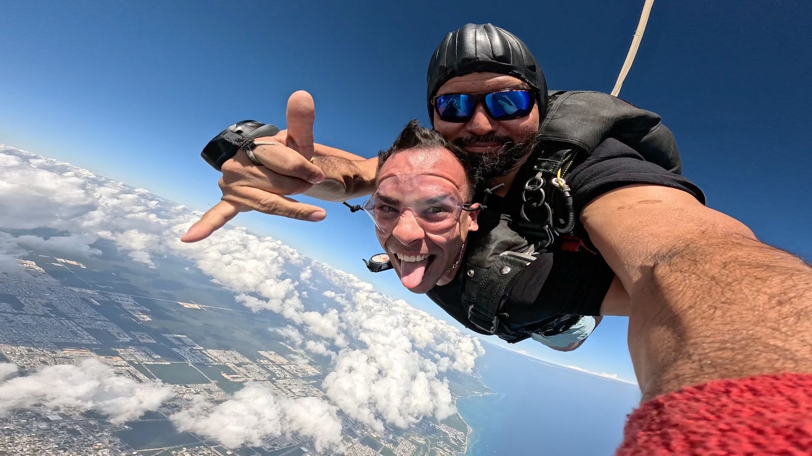 Two men smiling in freefall over the Cancun coastline with turquoise water stretching below