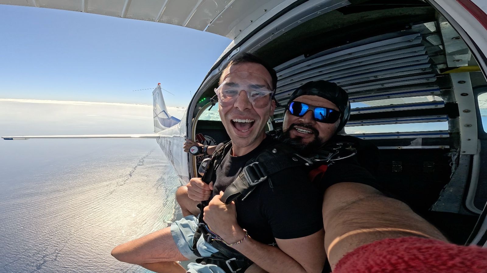 Two men laughing at the open aircraft door ready to jump over the Caribbean Sea