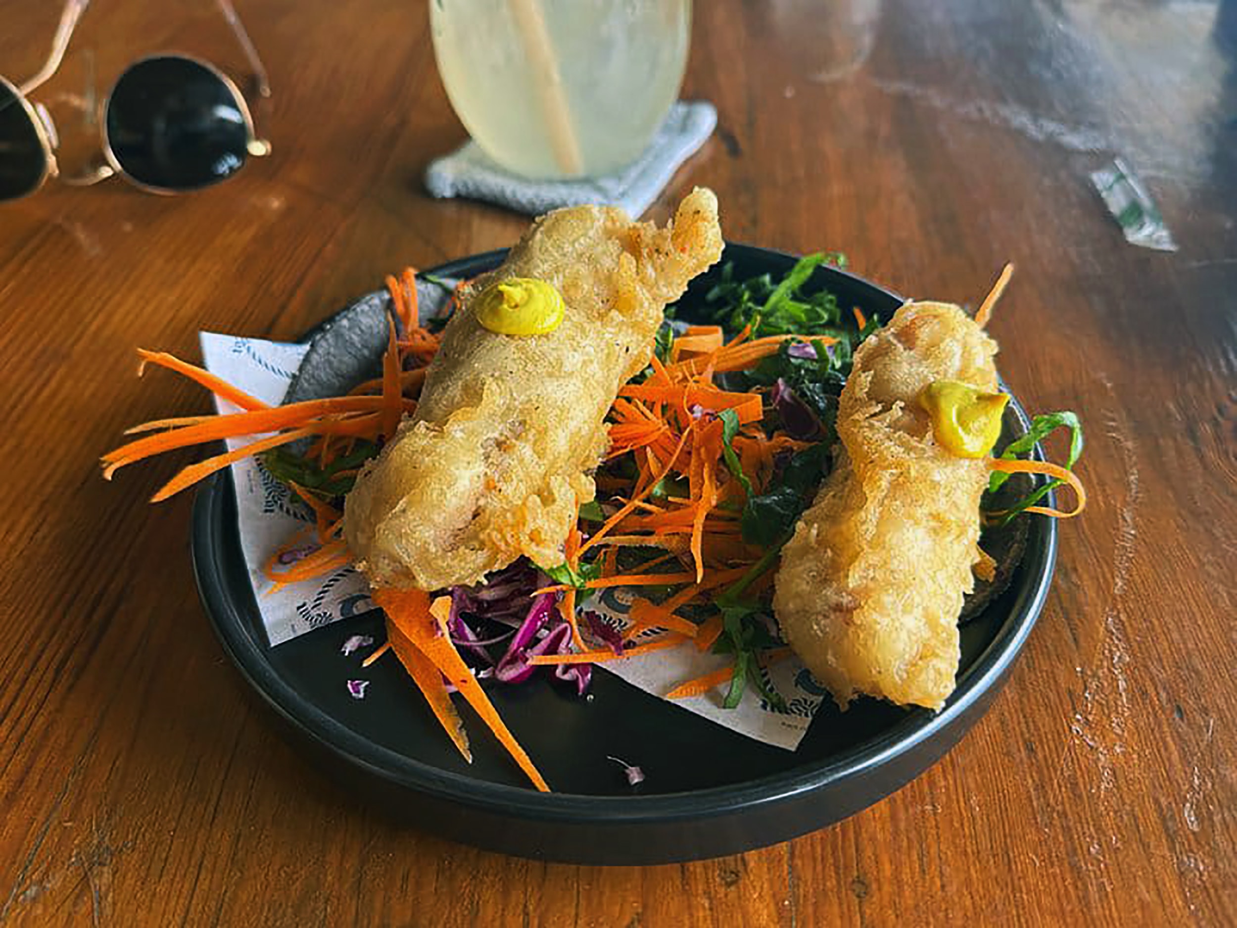 Crispy fried shrimp skewers on a black plate with shredded carrot salad at a Puerto Morelos beachside restaurant