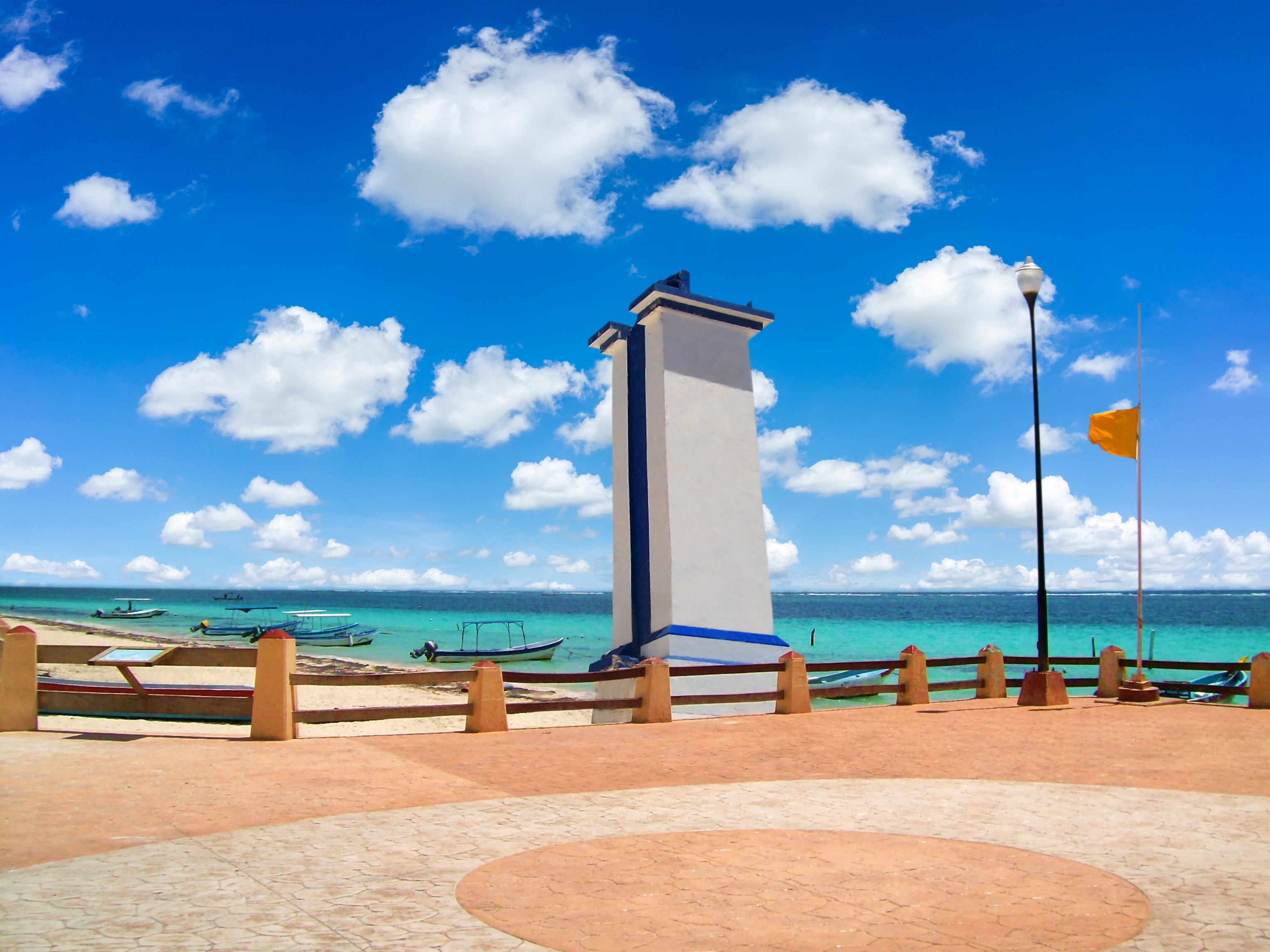 Puerto Morelos lighthouse and malecon promenade with fishing boats moored in turquoise Caribbean water under a blue sky