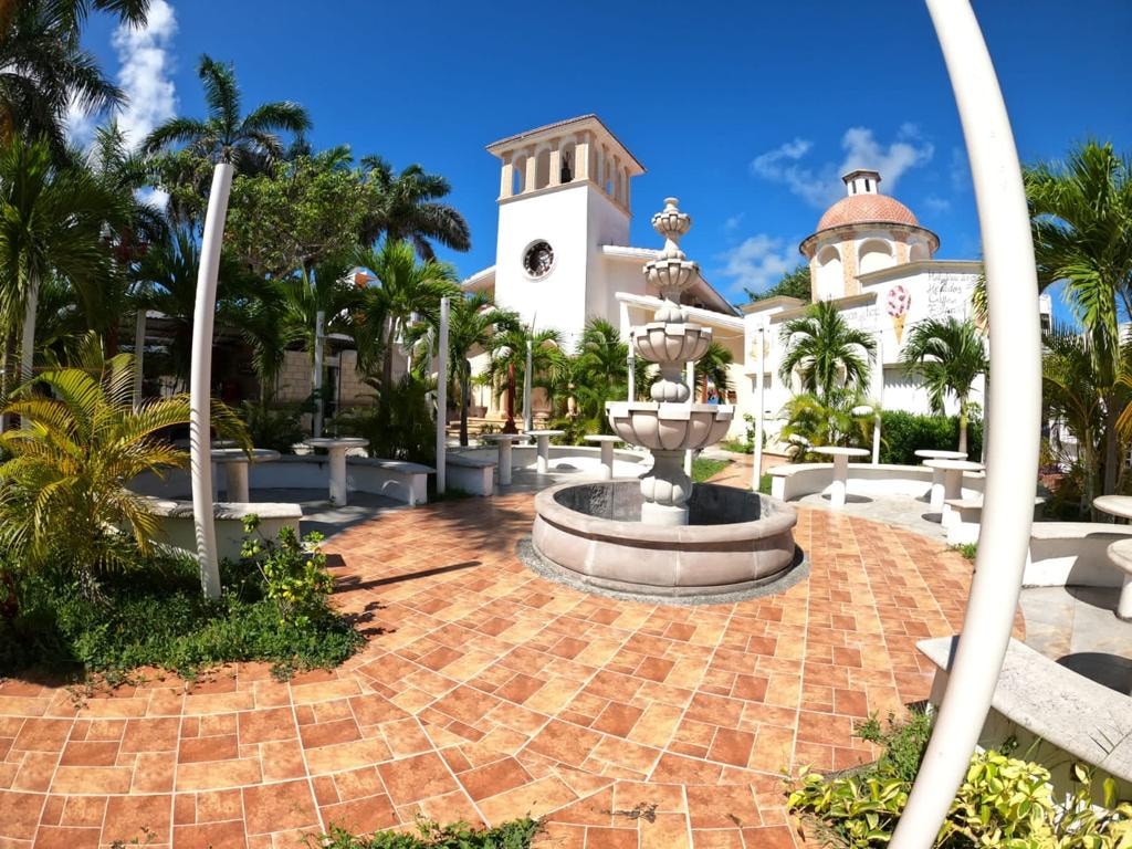 Puerto Morelos town plaza with a stone fountain, palm trees and the white colonial church on a sunny day