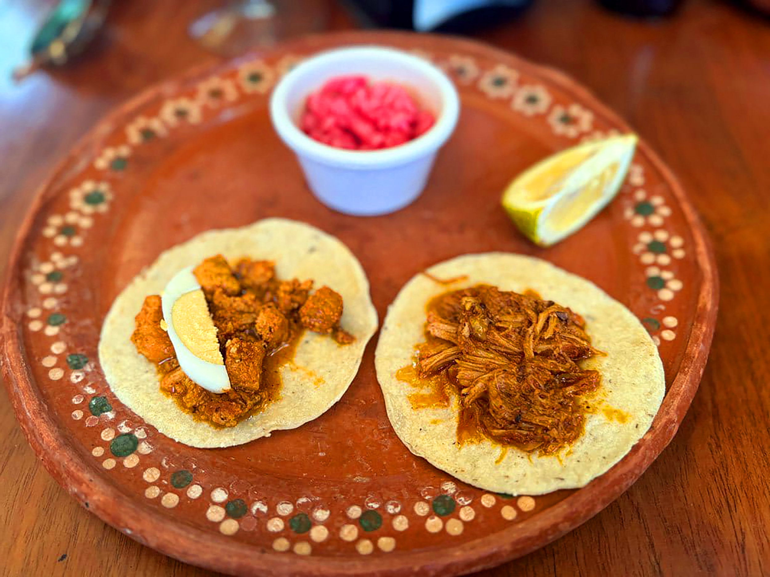 Traditional Mexican tacos on a hand-painted clay plate with cochinita pibil, pickled onions and lime at a Puerto Morelos restaurant
