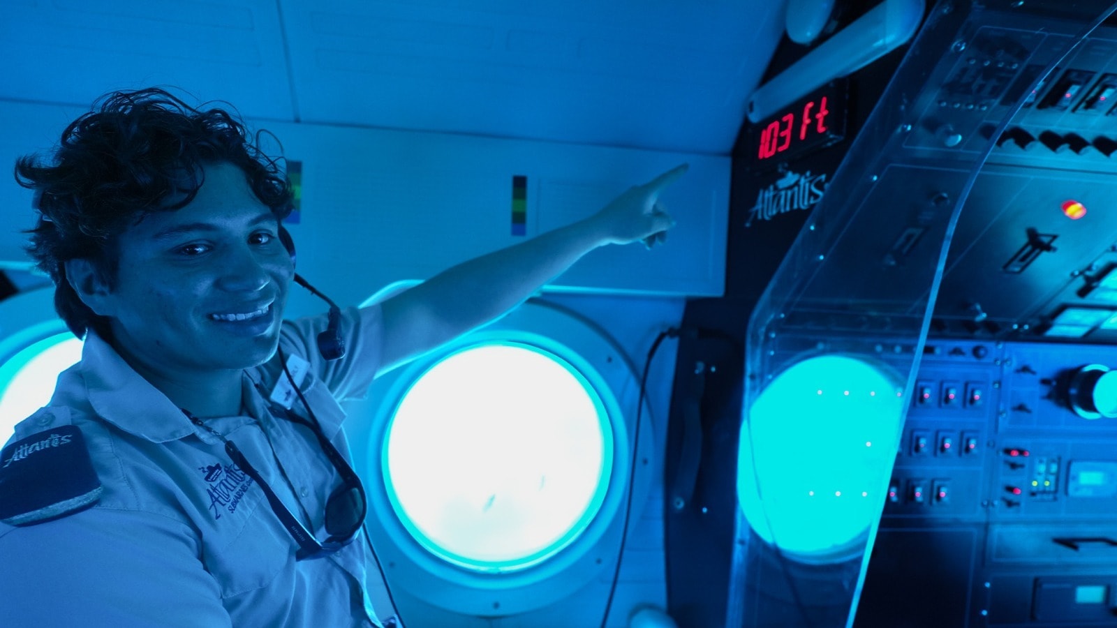 Atlantis Submarines Cozumel guide pointing at the 103 ft depth display inside the blue-lit cabin of the Atlantis XII