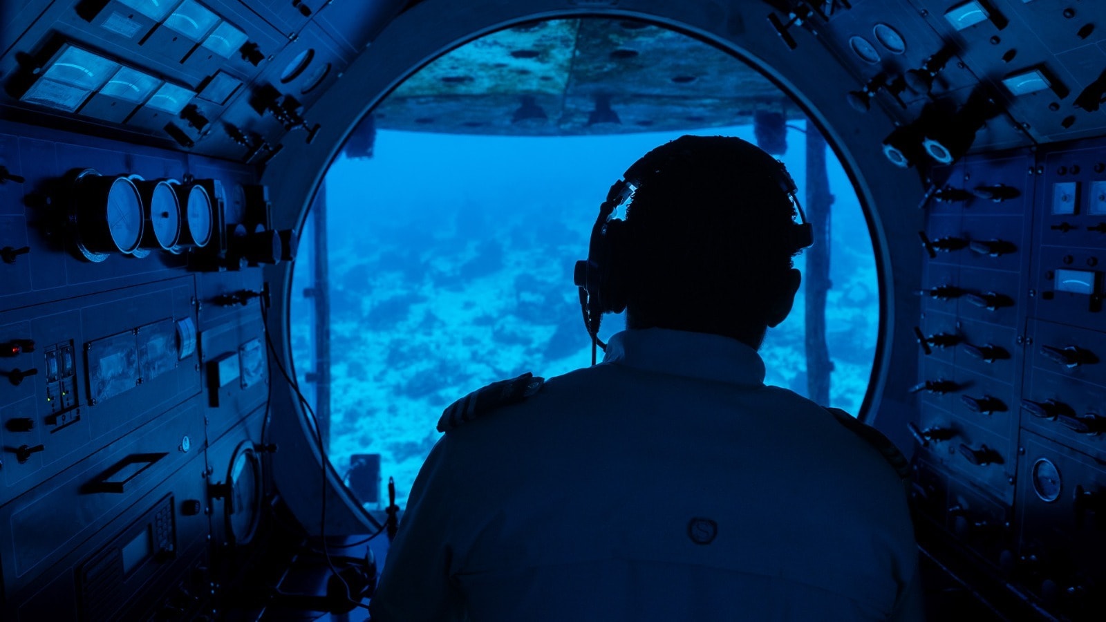 Silhouette of the Atlantis XII submarine pilot looking through the circular porthole at the Chankanaab Reef 100 feet below the surface