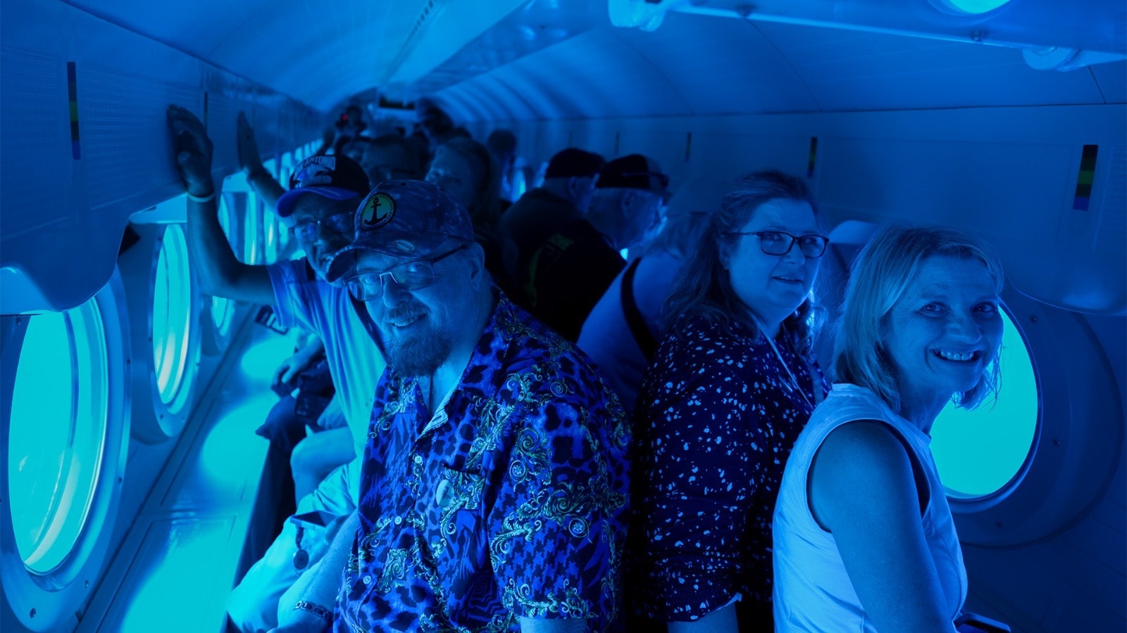 Group of passengers in the blue-lit cabin of the Atlantis XII submarine enjoying the underwater views in Cozumel