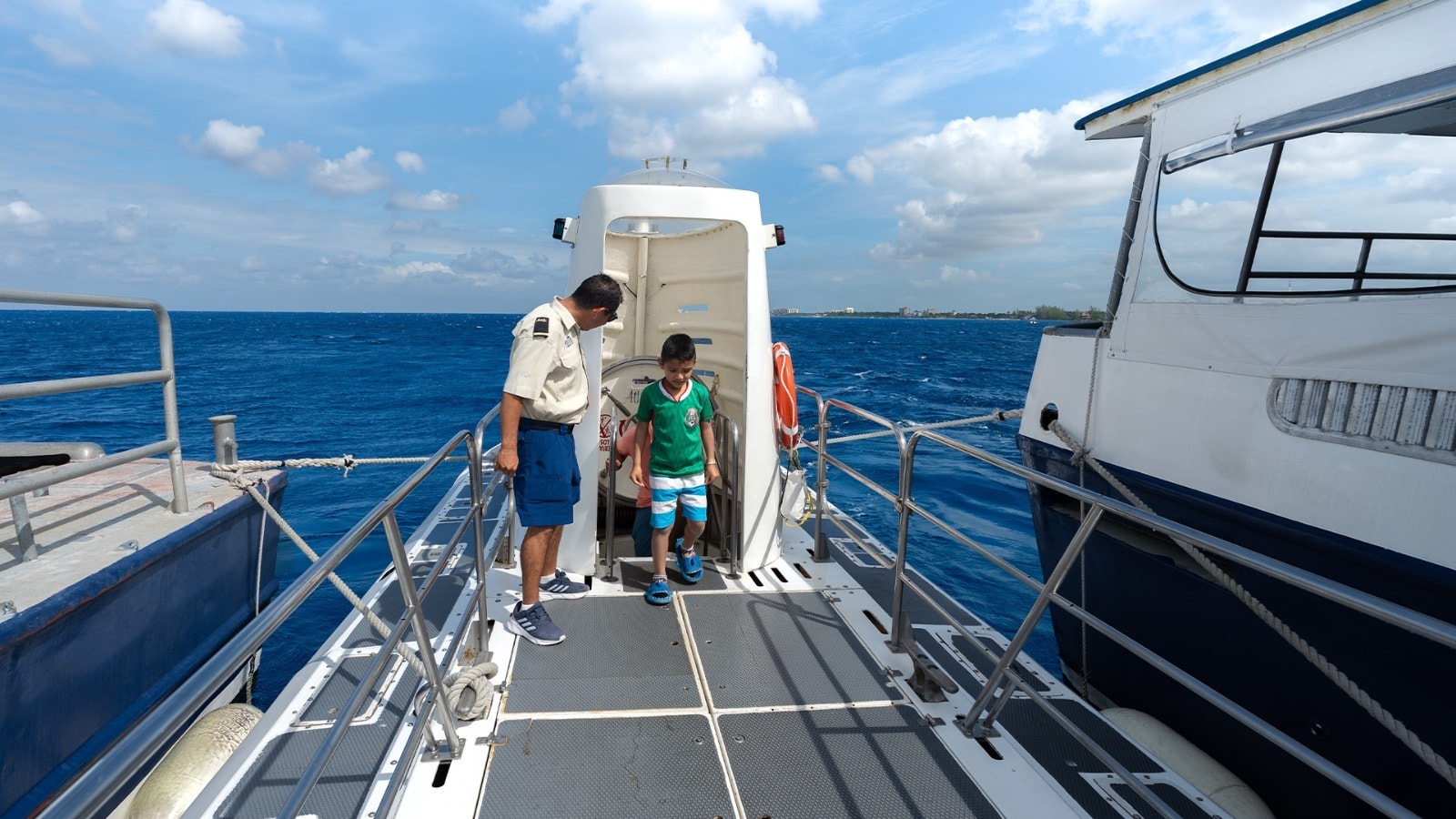 Atlantis crew member helping a young boy board the submarine on the open deck with the Caribbean Sea in the background