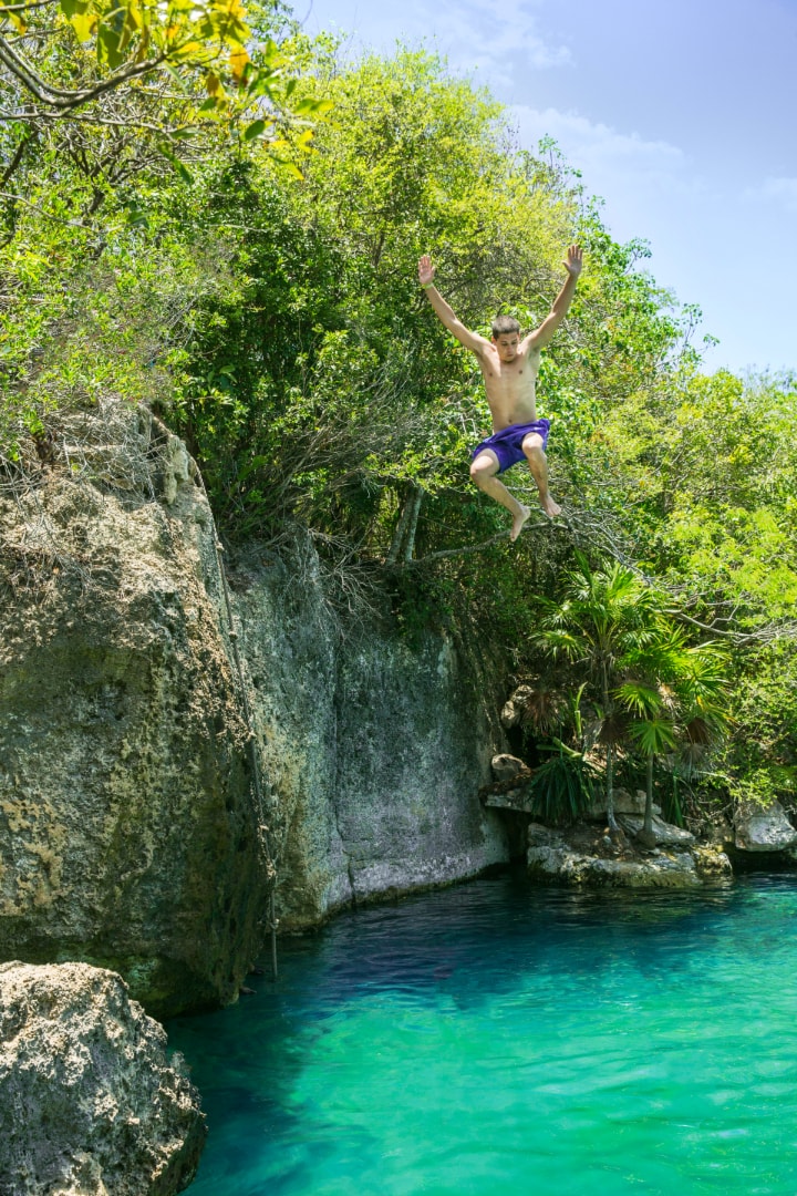 Young man cliff-jumping into crystal-clear turquoise water at Xel-Há