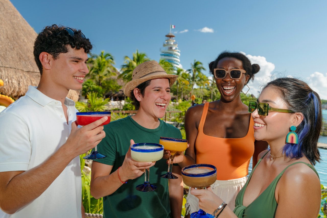 Four friends toasting with margaritas at Xel-Há with the lighthouse tower in the background