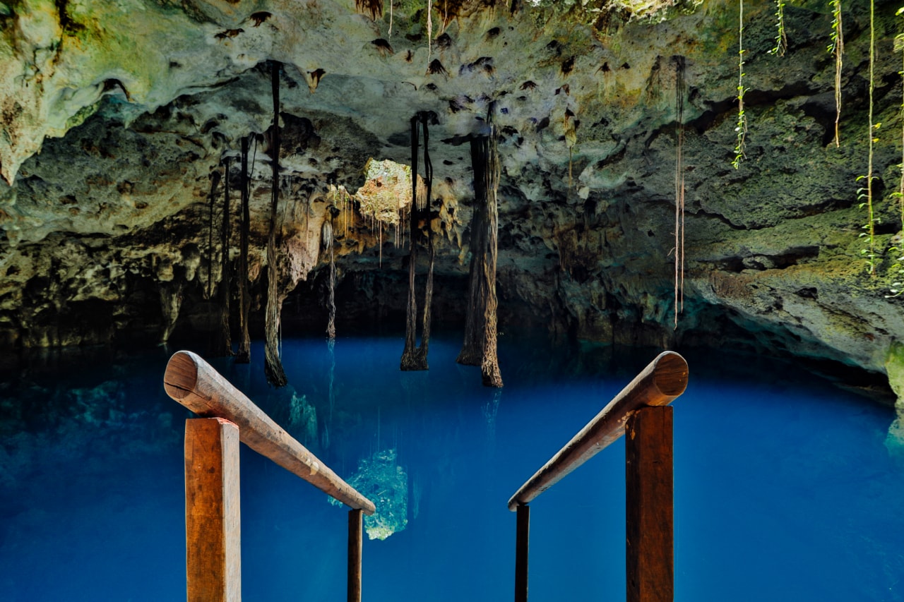 Stunning cave cenote with deep blue water, stalactites and wooden handrails at Xenotes Oasis Maya