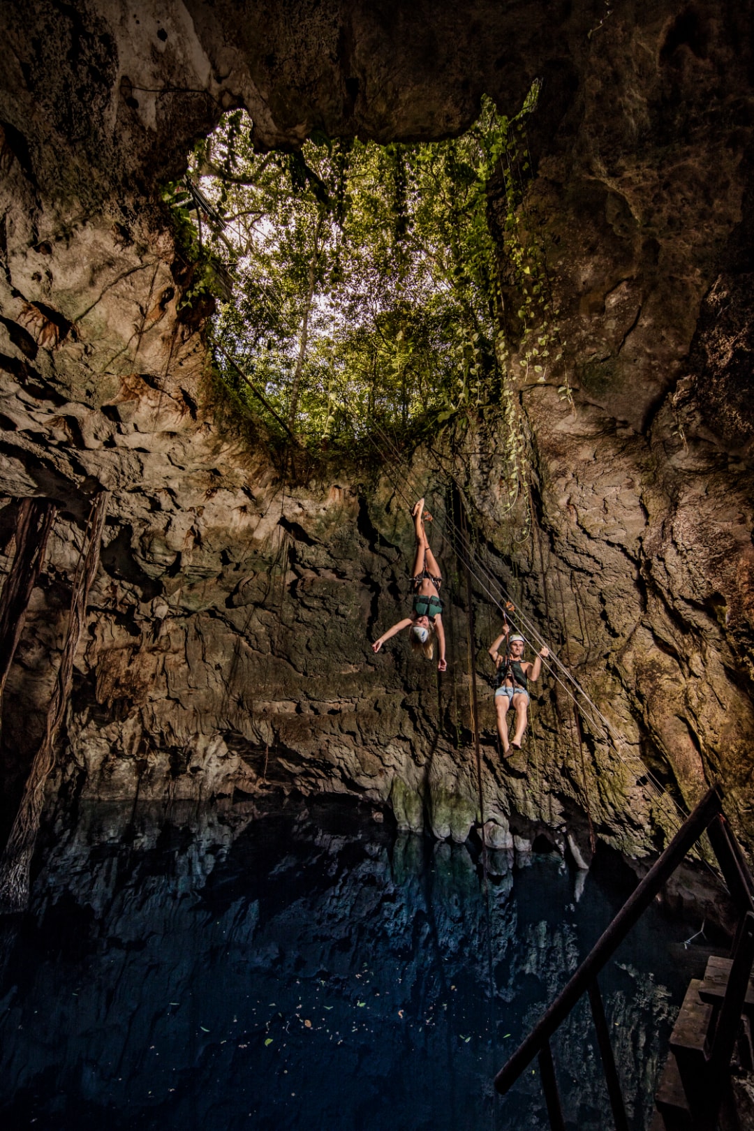 Two guests rappelling into a deep cave cenote with light streaming through the opening at Xenotes Oasis Maya