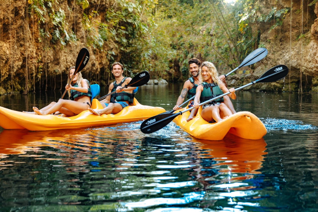 Two couples kayaking in yellow kayaks through a scenic jungle cenote channel at Xenotes Oasis Maya