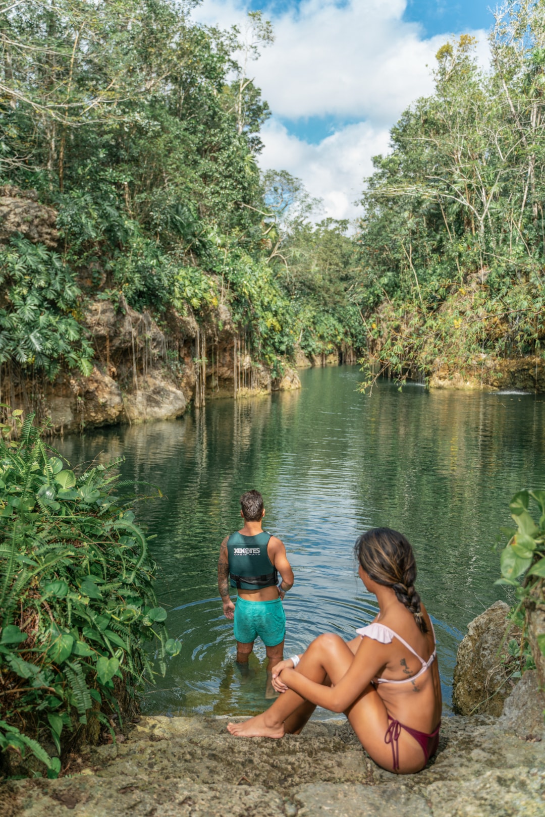 Couple relaxing at the edge of a tranquil open cenote surrounded by lush jungle at Xenotes Oasis Maya