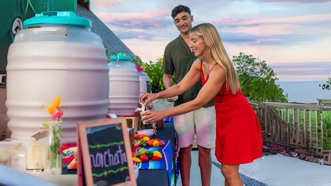 Couple serving themselves horchata at a welcome drinks station with a sunset sky at Xoximilco