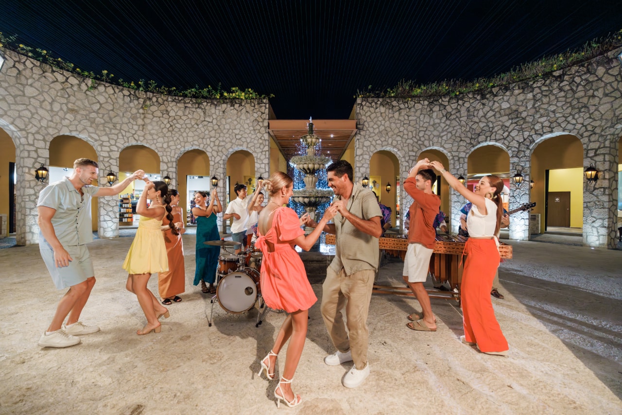 Couples dancing in a stone courtyard with a fountain and live marimba band at Xoximilco
