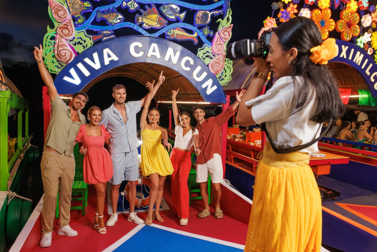 Group of friends posing under the Viva Cancún arch on the colourful Xoximilco trajinera at night