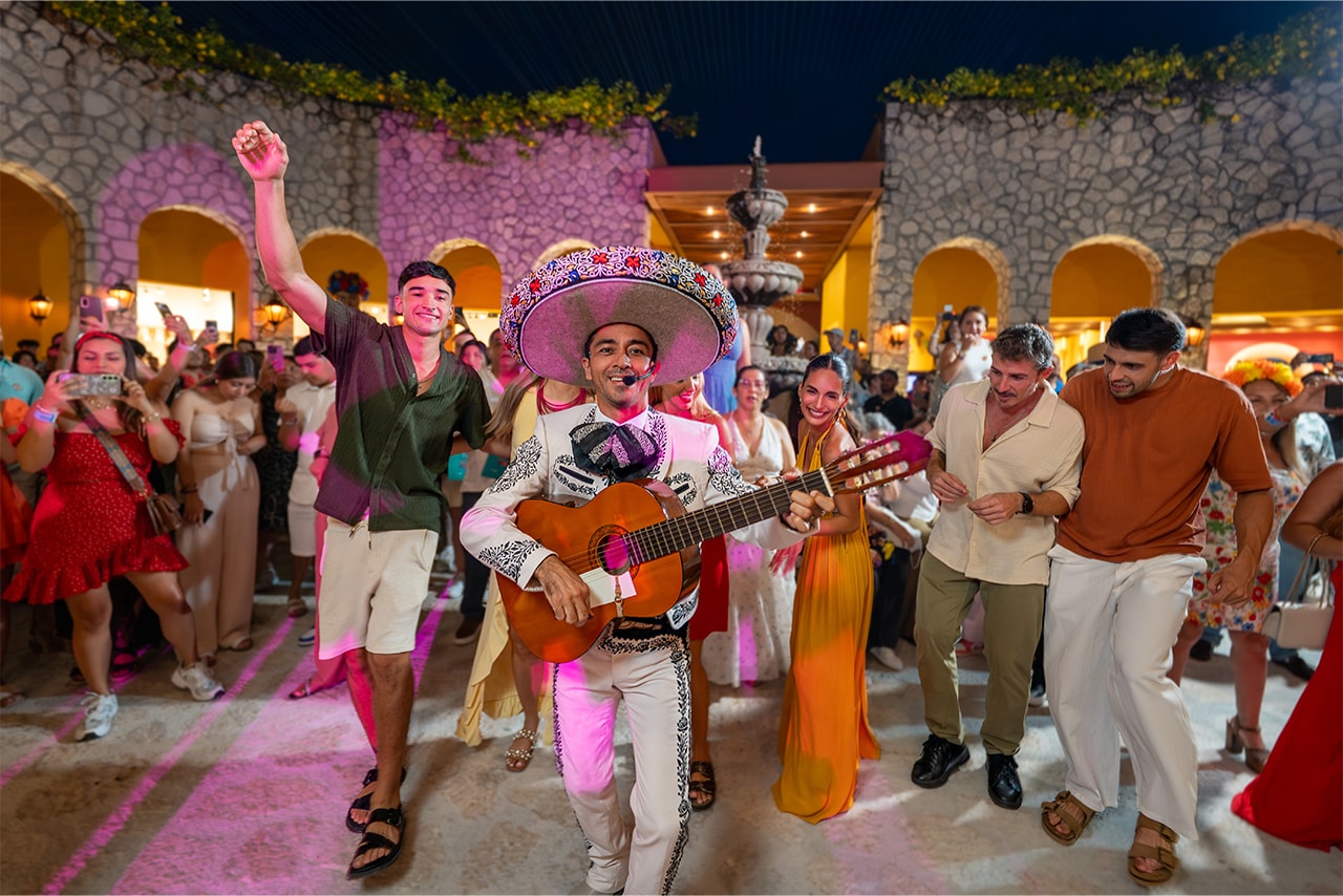 Mariachi singer in a sombrero leading a crowd of dancing guests through the Xoximilco courtyard